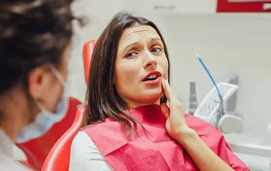 A woman looking at her dentist while holding her cheek in pain